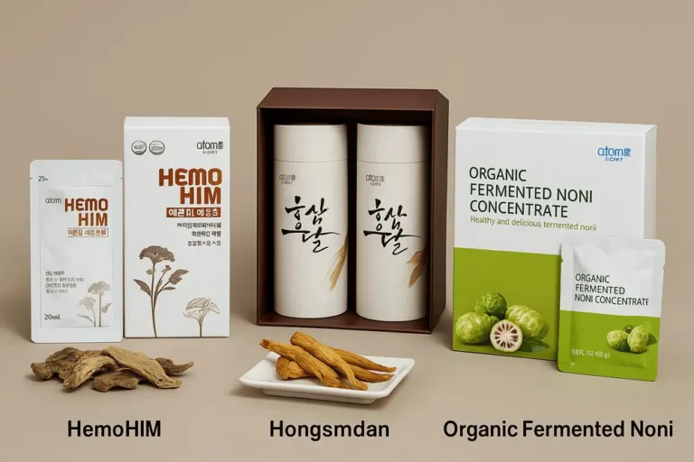 A digital photograph displays three Atomy health s compléments alimentaires Atomy — HemoHIM, Hongsamdan et Organic Fermented Noni Concentrate — disposés sur un fond beige, entourés de racines séchées et de fruits, avec le nom de chaque produit mentionné en dessous.